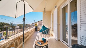 Un balcón con una hamaca colgante, una mesa con croissants y vistas al mar y edificios.