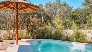 Una piscina con una cerca de bambú, una sombrilla de madera y un muro de piedra al fondo.