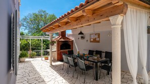 Um pátio externo com forno de tijolos, uma mesa com cadeiras e uma estrutura de pérgola.