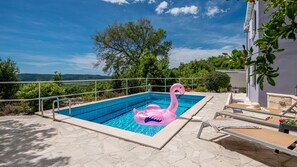 Uma piscina retangular com um flutuador de flamingo rosa, rodeada por ladrilhos de pedra e grades de metal.