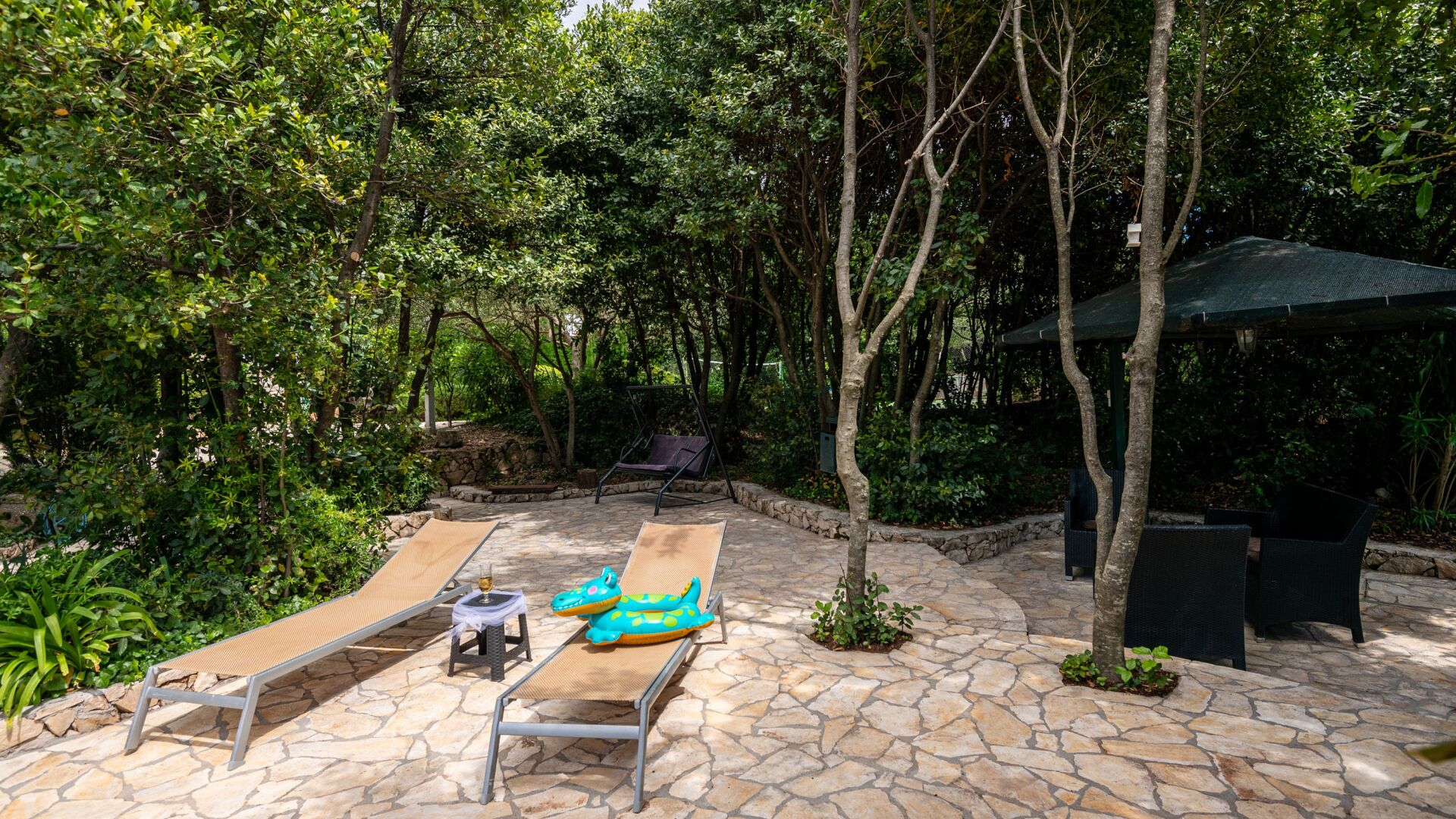 An outdoor patio with stone flooring, two lounge chairs, a small table, and a swing chair.