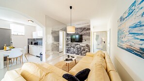 A modern living room with a sofa, a dining area with a table and chairs, a kitchen, and a TV mounted on the wall. - Villa Soldo by Villas Guide (Hodilje)