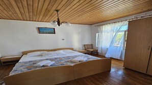 Een houten bed met een bedsprei met dessin, een houten plafond, een klein tafeltje met een stoel en een kledingkast.