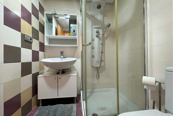 Un baño con pared de baldosas a cuadros, un lavamanos, un espejo, una cabina de ducha y un inodoro.