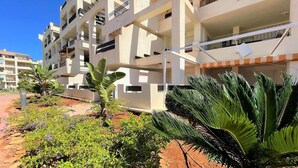 A multi-story residential building with balconies, surrounded by lush greenery and a well-maintained garden.