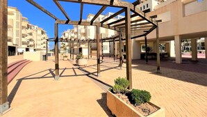 A courtyard with a wooden pergola structure, potted plants, and a paved walkway.