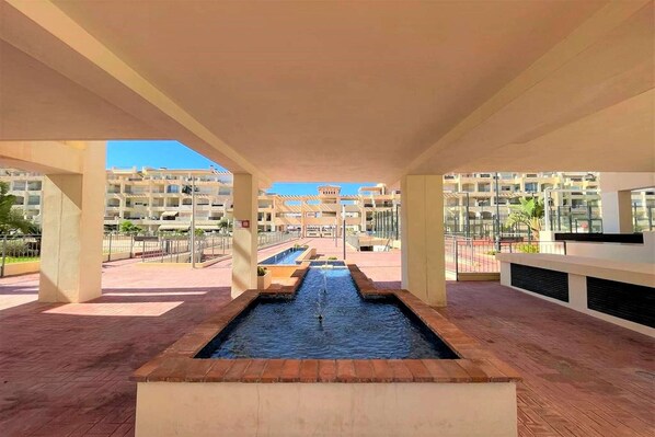Un moderno vestíbulo de hotel con una fuente central, varios balcones y vistas claras de los edificios circundantes.