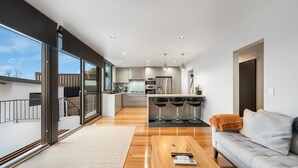 A modern kitchen with a central island, bar stools, and a dining area with a sofa and coffee table.