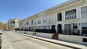 A row of white buildings with balconies, a clear sky, and a street in the foreground.