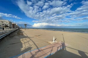 A beach with a wooden walkway, palm trees, and a building in the background.