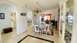A dining area with a chandelier, white chairs, and a glass cabinet with dishes. - Holiday home near the beach on the Costa Tropical (Calahonda)