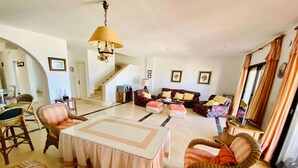 A spacious living room with a large table, wicker chairs, a sofa set, and a staircase leading to another level. - Holiday home near the beach on the Costa Tropical (Calahonda)