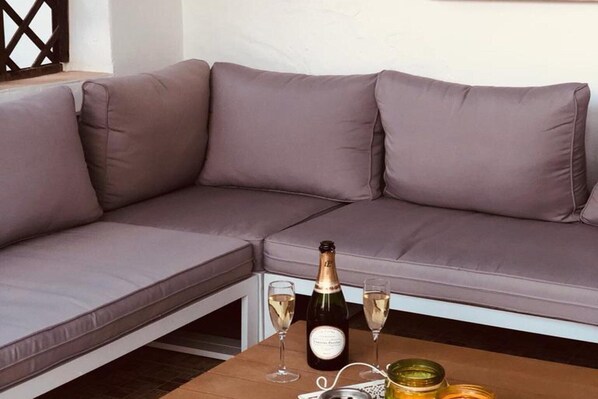 Un canapé d’angle avec des coussins, une bouteille de champagne, deux verres et une petite table avec une bougie et un pot.