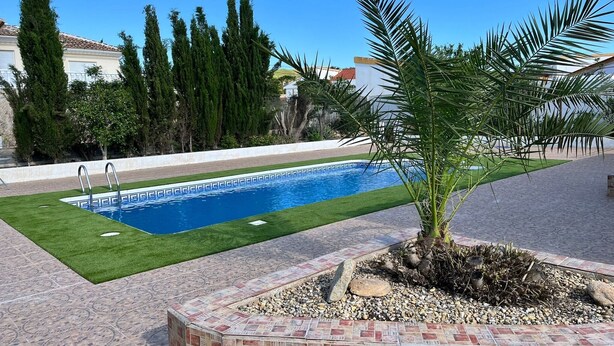 Una piscina con agua cristalina azul, rodeada por un césped bien cuidado y diversas especies de árboles.