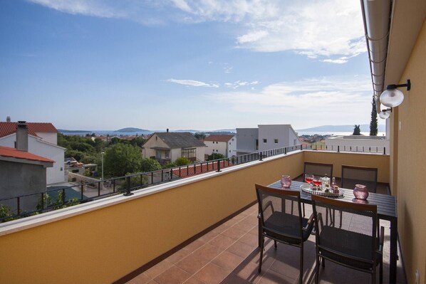 A balcony with a table and chairs, overlooking a residential area with houses and a distant view of hills.
