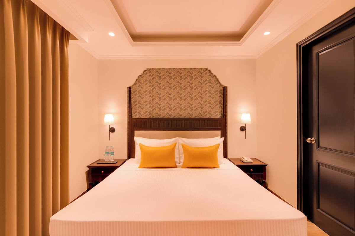 Una habitación de hotel con una cama grande, dos mesitas de noche, un cabecero con diseño estampado y una puerta a la derecha.