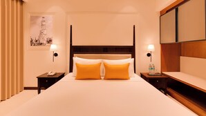 A hotel room with a four-poster bed, two bedside tables, a nightstand, a wall-mounted lamp, a framed picture, and a wooden panel on the wall.