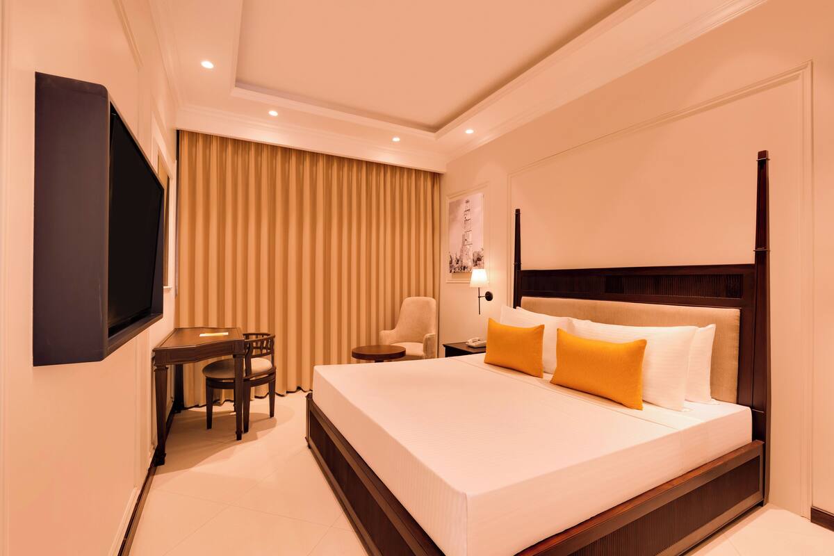 Una habitación de hotel con una cama grande, un escritorio, una silla, un televisor y una lámpara.