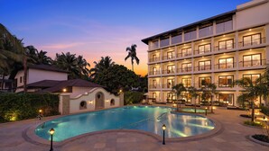 A pool area with a curved design, surrounded by a multi-story building with balconies and a well-lit exterior.