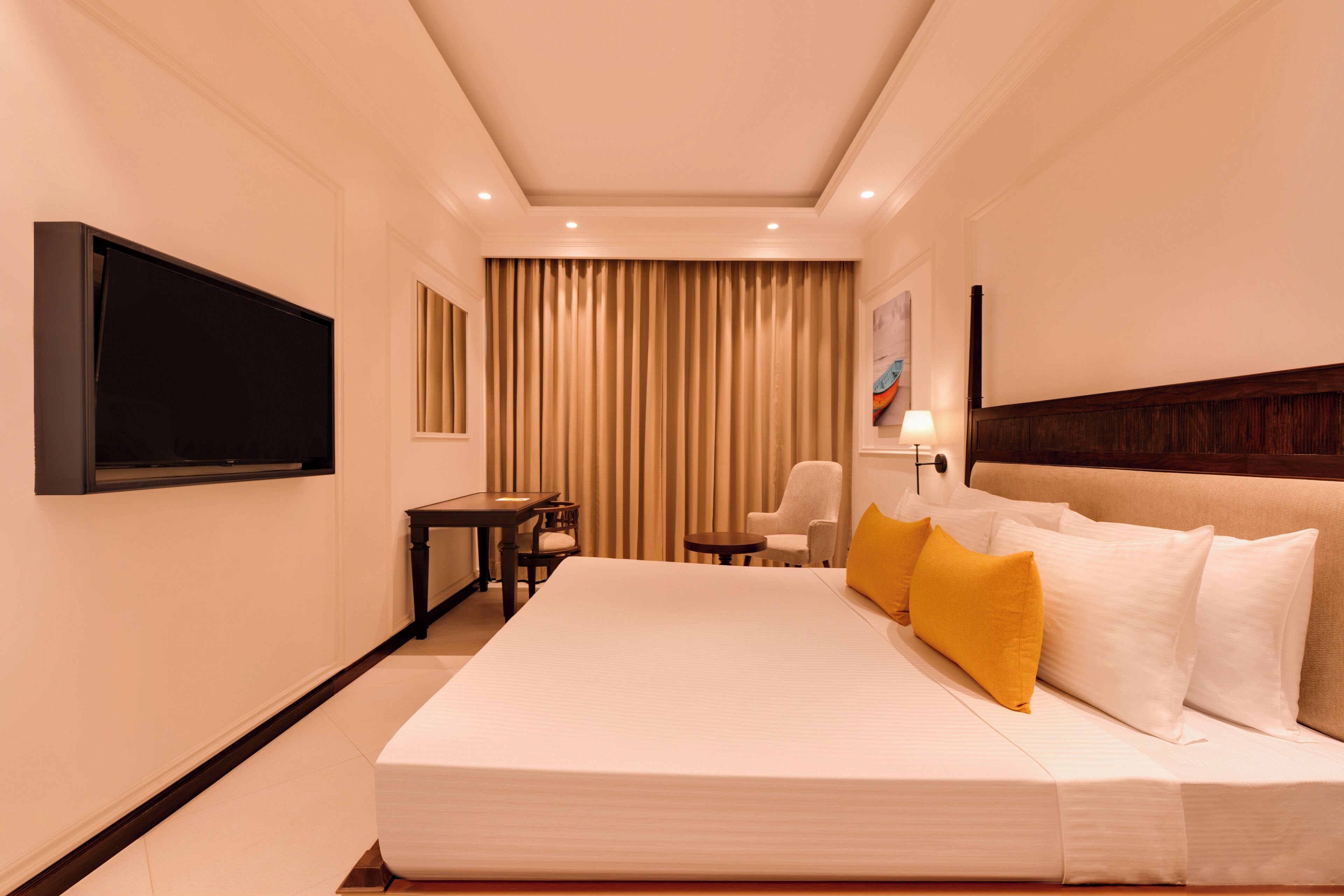 Una habitación de hotel con una cama grande, un televisor de pantalla plana montado en la pared, un escritorio con silla y una ventana con cortinas.