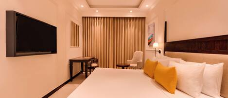 Una habitación de hotel con una cama grande, un televisor de pantalla plana montado en la pared, un escritorio con silla y una ventana con cortinas.