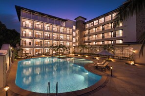 Un hôtel à plusieurs étages doté d’une piscine, d’un espace extérieur aménagé et de balcons bien éclairés.