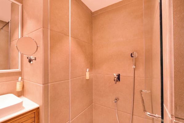 A bathroom with beige tiles, a round mirror, a sink with a wooden cabinet, and a shower with a handheld showerhead.