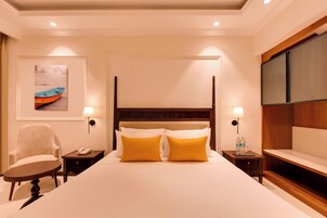 Habitación de hotel con una cama grande, dos mesitas de noche, una silla, un cuadro y un panel de madera en la pared.