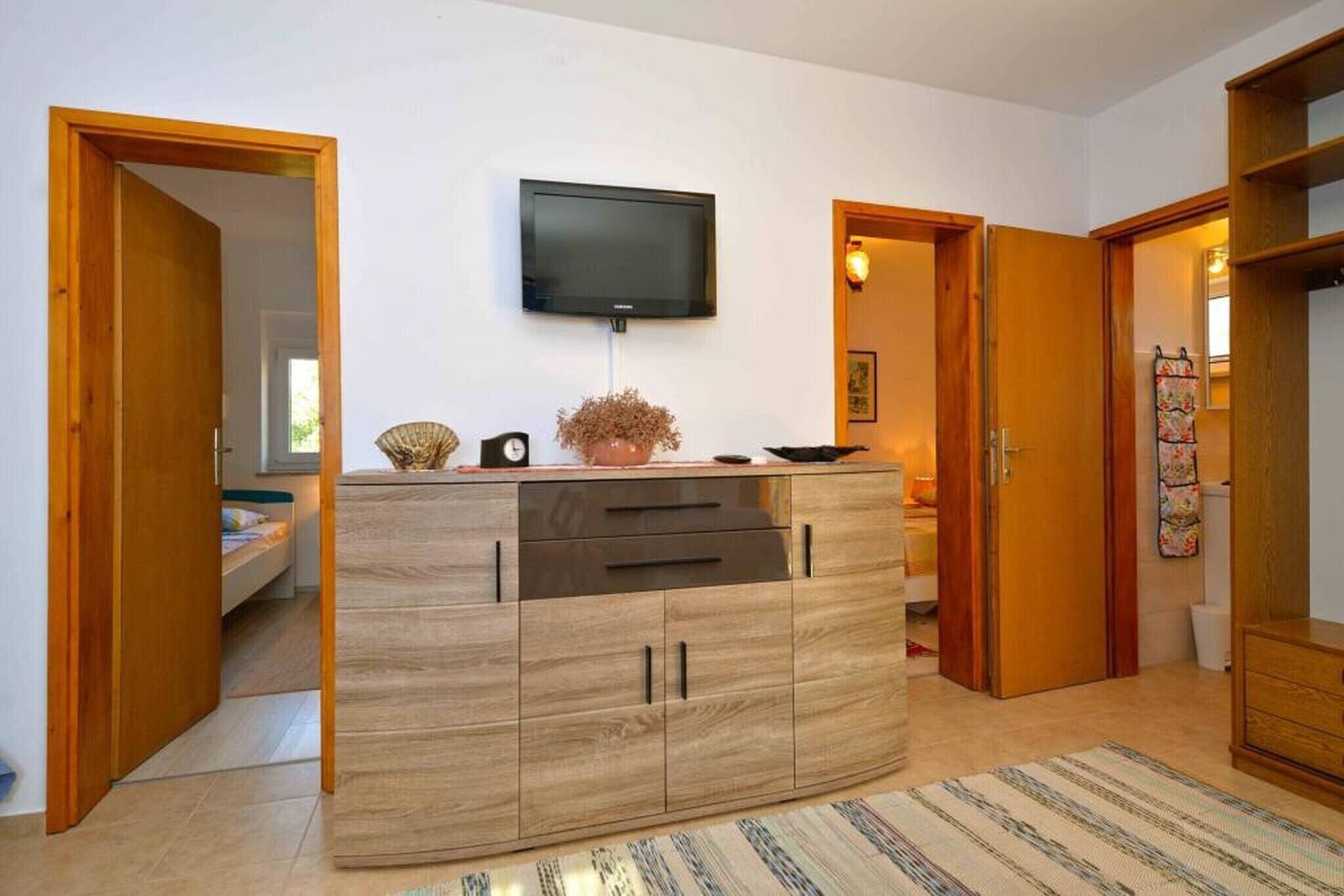 A modern living room with a wooden cabinet, a flat-screen TV mounted on the wall, and a door leading to another room.