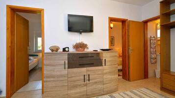 A modern living room with a wooden cabinet, a flat-screen TV mounted on the wall, and a door leading to another room.