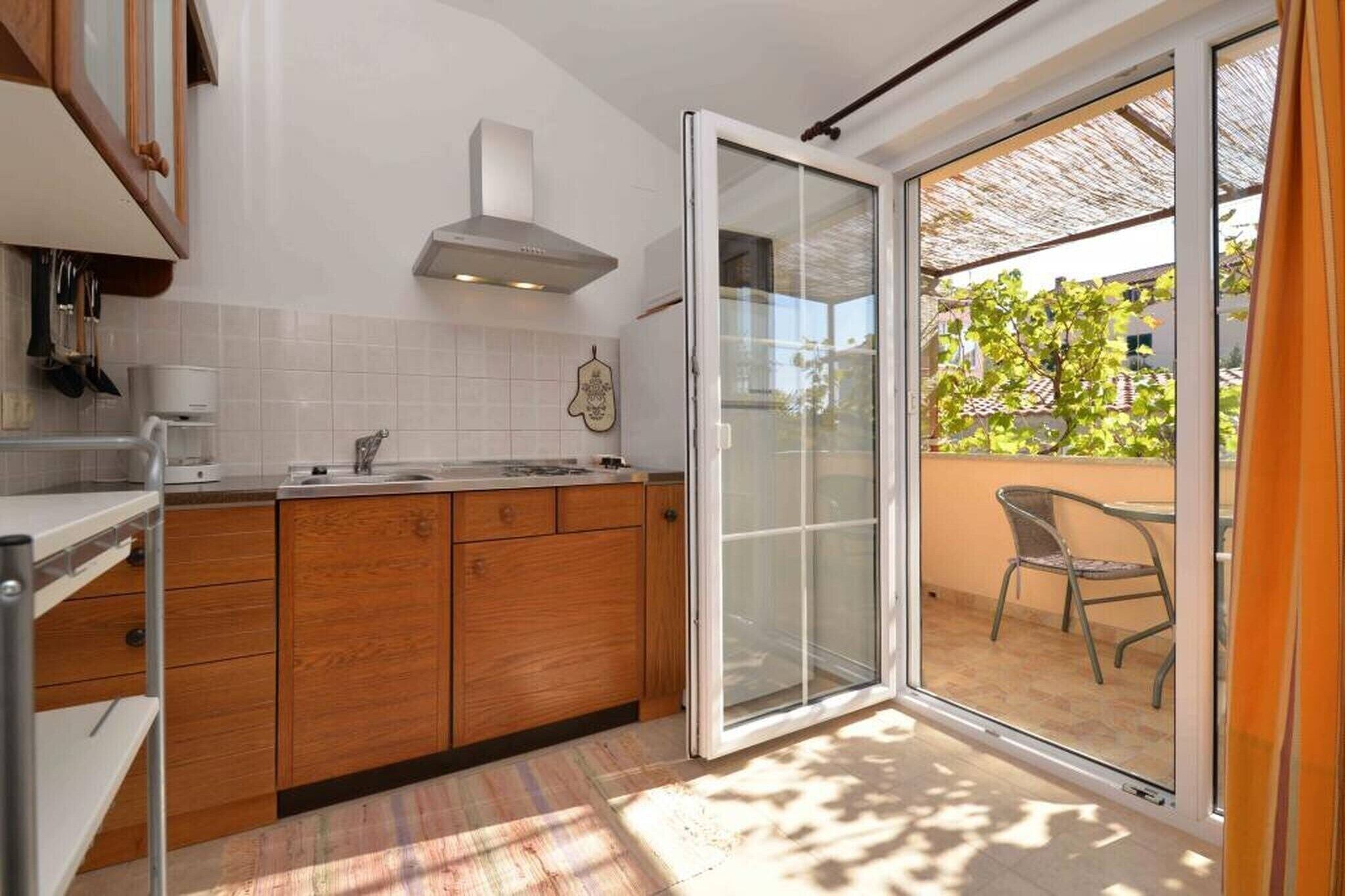 A kitchen with wooden cabinets, a white countertop, and a built-in oven. There is a sliding glass door leading to an outdoor patio with a table and chairs.