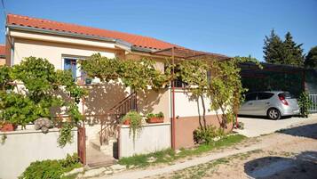 A residential building with a red-tiled roof, a car parked in the driveway, and a garden with vines and plants.