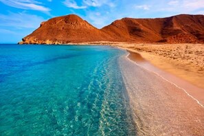 A beach with clear turquoise water, sandy shore, and a mountain in the background. - Belvilla by OYO Apartamento VerandaMar Sandra (Almeria)
