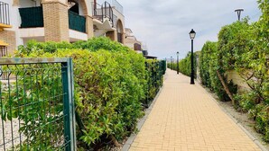 A paved pathway flanked by greenery and a building with arched windows and balconies.