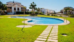 A swimming pool with a clear blue water, surrounded by a well-maintained lawn and a paved walkway.
