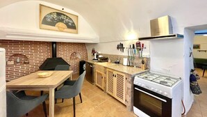 A compact kitchen with a gas stove, a brick wall, and a dining area with a table and chairs. - Cave House in Cúllar near Tabernas Desert (Cúllar)