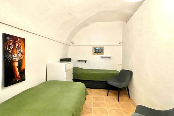 A small, cozy room with two beds, a chair, a small desk, and a painting of a tiger.