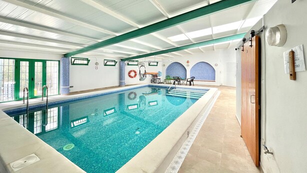 A large indoor swimming pool with clear water, surrounded by a tiled floor and a high ceiling with green beams. - Cave House in Cúllar near Tabernas Desert (Cúllar)