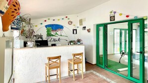 A reception area with a white counter, two wooden chairs, a green door, and a wall mural. - Cave House in Cúllar near Tabernas Desert (Cúllar)