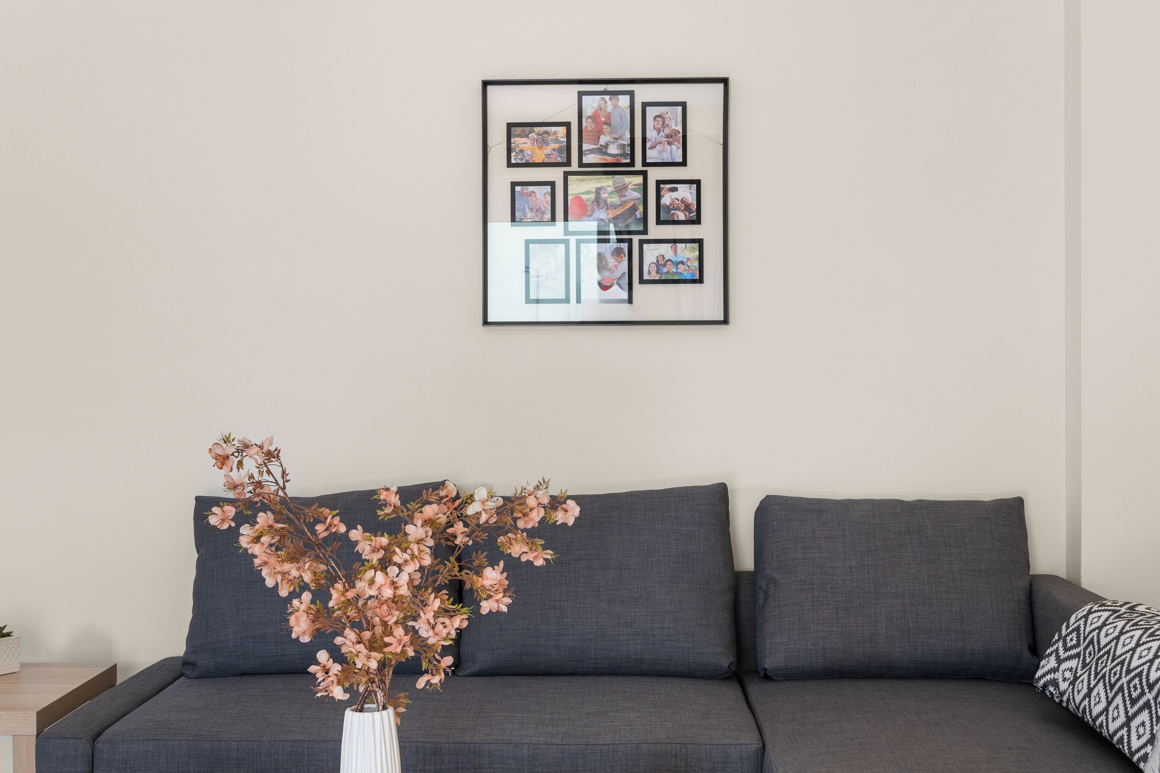 A modern living room with a grey sofa, a framed photo collage on the wall, and a vase with pink flowers on a side table.