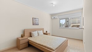 Ein Schlafzimmer mit einem Bett, Nachttischen, einer Wand-Klimaanlage und einem Fenster mit Blick nach draußen.