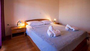 A neatly made bed with white linens and towels, a bedside lamp, and a wooden nightstand.