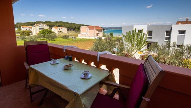 A balcony with a table and chairs, overlooking a coastal area with buildings and greenery.