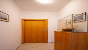 A hallway with a wooden door, a tiled floor, and a glass display cabinet with a ship model.