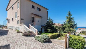 A two-story building with a tiled roof, a staircase leading to the entrance, and a view of the sea in the background. - Beautiful apartment near Rtić beach (Primošten)