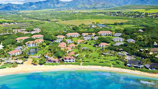 Une station balnéaire dotée de villas en bord de mer, d’une végétation luxuriante et d’un paysage montagneux en toile de fond.
