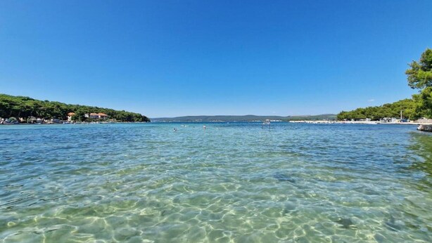 Ein klarer Blick auf einen stillen See mit einer entfernten Uferlinie, umgeben von Grünflächen und Gebäuden.