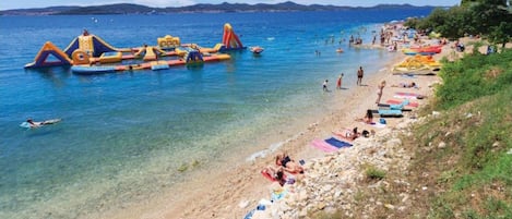 A beach with inflatable water toys, clear blue water, and people sunbathing.