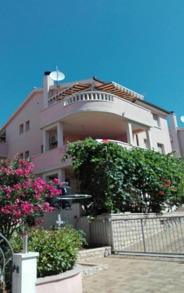 A multi-story residential building with a balcony, satellite dish, and potted plants.