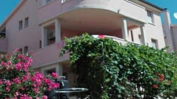 Un edifici residencial de diversos pisos amb un balcó, una antena parabòlica i plantes en testos.